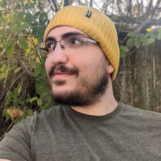 Kaan, wearing a beanie, in front of some shrubbery.